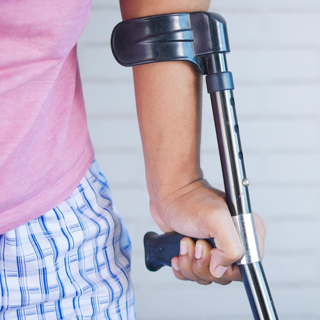 A person with crutches is holding onto the handle of their walking stick.