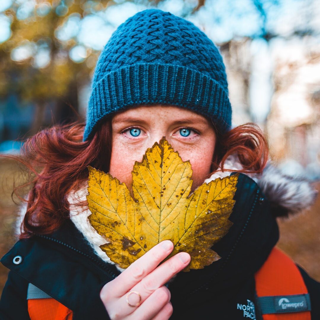 A woman holding a leaf in front of her face.