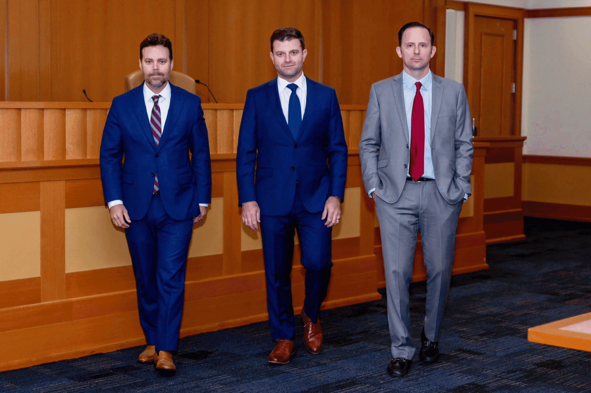 Three men in suits walking in courtroom.