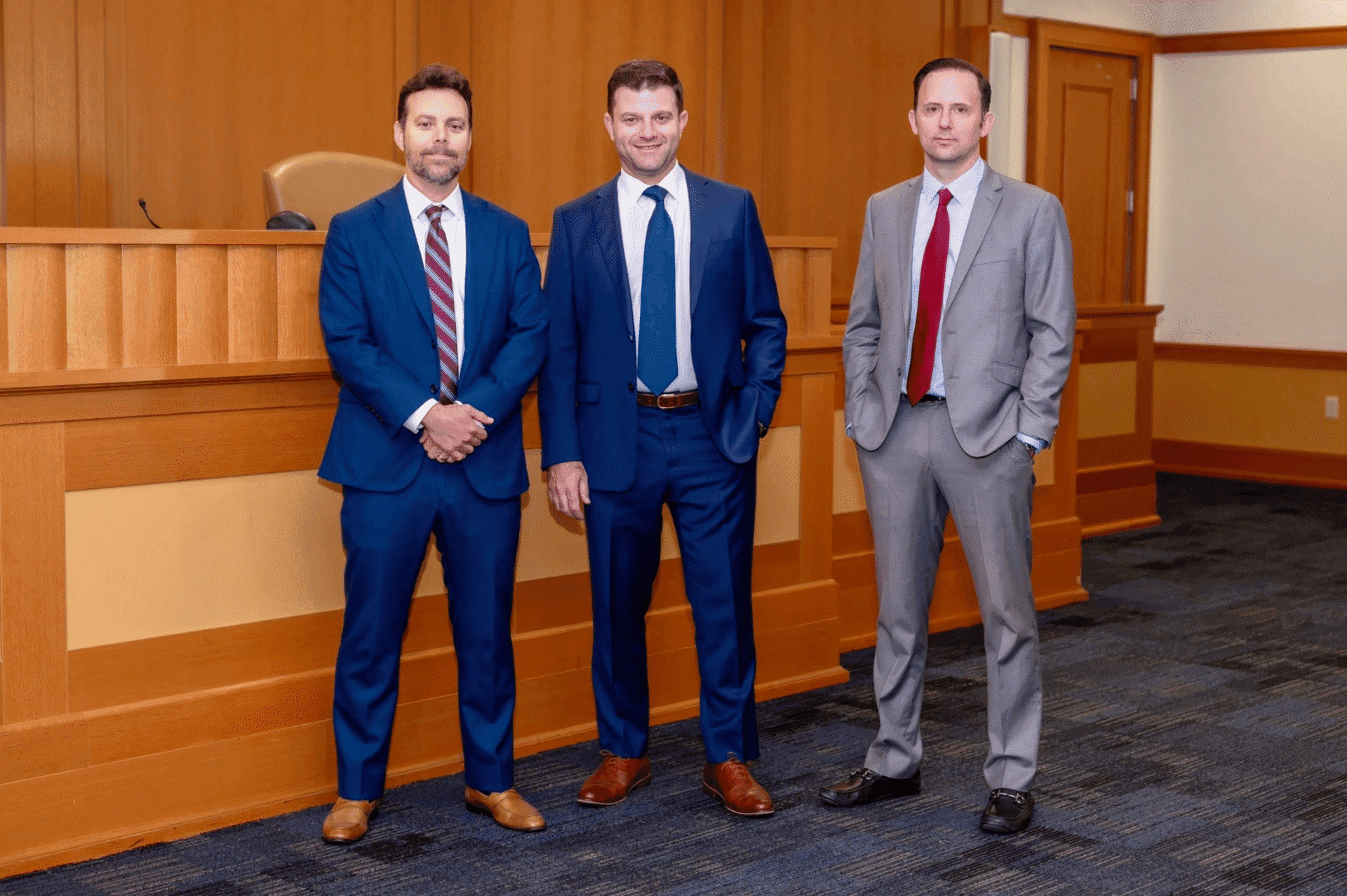 Three men in suits standing in courtroom.